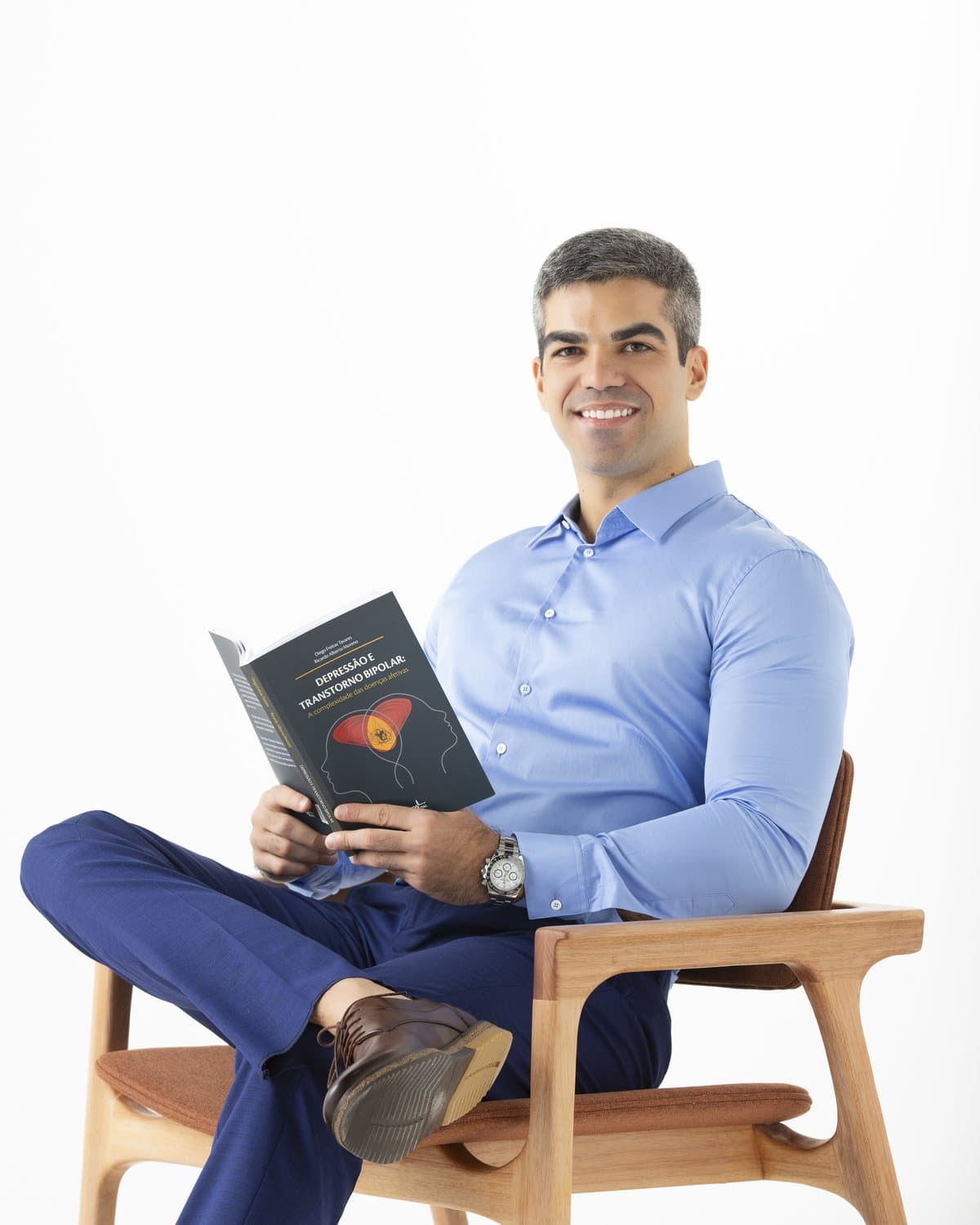 Dr. André Garcia sentado em uma poltrona, com um livro nas mãos